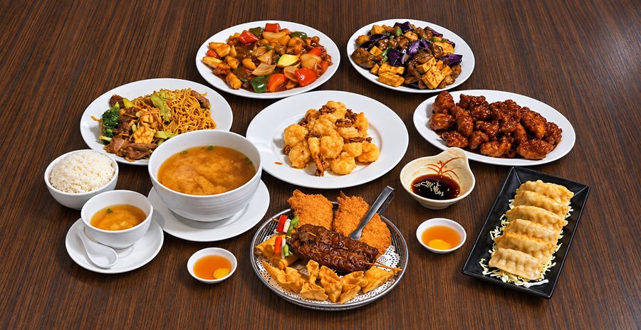A spread of Chen's dishes on a wood table: honey walnut shrimp, orange chicken, chow mein, stir-fried entr&eacute;es, soup, steamed rice, a fried appetizer platter and pot stickers.